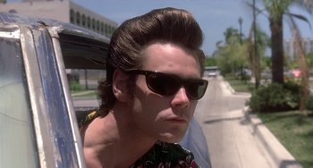 Movie still from “Ace Ventura: Pet Detective” (1994), directed by Tom Shadyac – A young man with sunglasses on a road; Close Up shot, Low angle