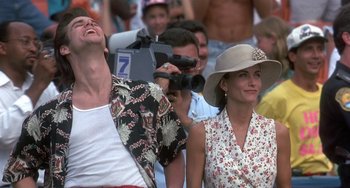 Movie still from “Ace Ventura: Pet Detective” (1994), directed by Tom Shadyac – A man and a woman in a crowd holding a video camera; Medium shot, Low angle