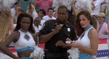 Movie still from “Ace Ventura: Pet Detective” (1994), directed by Tom Shadyac – A man in a police uniform with two cheerleaders; Close Up shot, Low angle