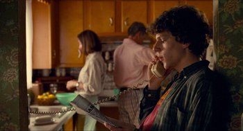 Movie still from “Adventureland” (2009), directed by Greg Mottola – A woman talking on a phone while holding a newspaper; Medium shot, Over the shoulder angle