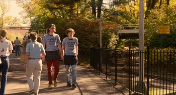 Movie still from “Adventureland” (2009), directed by Greg Mottola – A group of people walking down a sidewalk near a bridge; Medium shot, Over the shoulder angle