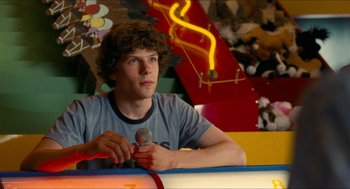 Movie still from “Adventureland” (2009), directed by Greg Mottola – A man sitting at a table holding a microphone in his hand; Close Up shot, Over the shoulder angle