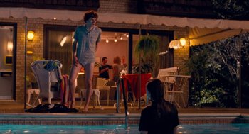 Movie still from “Adventureland” (2009), directed by Greg Mottola – A man standing in a swimming pool next to a woman; Wide shot, Over the shoulder angle