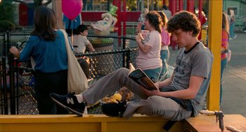 Movie still from “Adventureland” (2009), directed by Greg Mottola – A man sitting on top of a bench reading a book; Medium shot, Over the shoulder angle