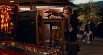 Movie still from “Adventureland” (2009), directed by Greg Mottola – A man standing in front of a pinball machine; Medium shot, Over the shoulder angle