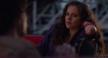 Movie still from “Adventureland” (2009), directed by Greg Mottola – A woman sitting on a red couch looking at the camera; Close Up shot, Over the shoulder angle