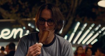 Movie still from “Adventureland” (2009), directed by Greg Mottola – A man with glasses is eating a piece of food; Close Up shot, Over the shoulder angle