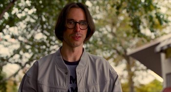 Movie still from “Adventureland” (2009), directed by Greg Mottola – A man with long brown hair wearing glasses and a gray jacket; Close Up shot, Over the shoulder angle