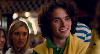 Movie still from “Adventureland” (2009), directed by Greg Mottola – A young man with long brown hair and a green shirt; Close Up shot, Over the shoulder angle