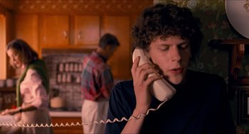 Movie still from “Adventureland” (2009), directed by Greg Mottola – A young man talking on a phone in a kitchen; Medium shot, Over the shoulder angle