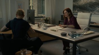 Movie still from “After the Wedding” (2019), directed by Bart Freundlich – Two people sitting at a table in front of computers; Medium shot, Over the shoulder angle