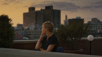 Movie still from “After the Wedding” (2019), directed by Bart Freundlich – A woman sitting on top of a building looking at the sky; Medium shot, Over the shoulder angle