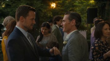 Movie still from “After the Wedding” (2019), directed by Bart Freundlich – Two men are shaking hands at an outdoor event; Medium shot, Over the shoulder angle