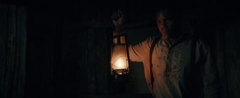 Movie still from “Alice” (2022), directed by Krystin Ver Linden – A man holding a lantern in a dark room; Medium shot, Low angle