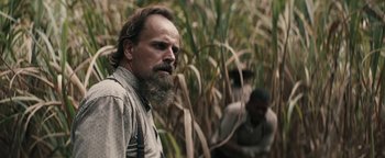 Movie still from “Alice” (2022), directed by Krystin Ver Linden – A man with a long beard standing next to a field; Close Up shot, Over the shoulder angle