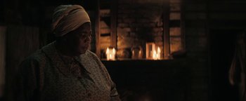Movie still from “Alice” (2022), directed by Krystin Ver Linden – An older woman sitting in front of a fireplace; Medium shot, Over the shoulder angle