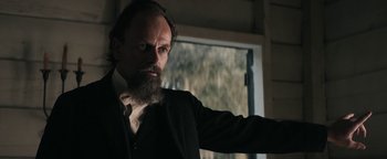 Movie still from “Alice” (2022), directed by Krystin Ver Linden – A man with a long beard is standing in front of a window; Close Up shot, Low angle