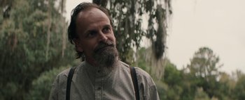 Movie still from “Alice” (2022), directed by Krystin Ver Linden – A man with a long beard wearing a gray shirt and suspenders; Close Up shot, Over the shoulder angle