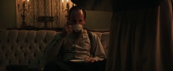 Movie still from “Alice” (2022), directed by Krystin Ver Linden – A man sitting on a couch drinking a cup of coffee; Medium shot, Low angle
