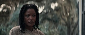 Movie still from “Alice” (2022), directed by Krystin Ver Linden – A woman with dreadlocks standing in front of a tree; Close Up shot, Low angle