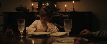 Movie still from “Alice” (2022), directed by Krystin Ver Linden – A young boy sitting at a table with a plate in front of him; Medium shot, High angle
