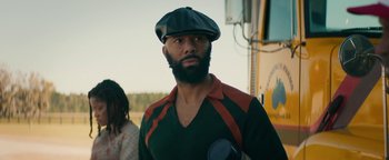 Movie still from “Alice” (2022), directed by Krystin Ver Linden – A man with a beard wearing a hat and suspenders standing in front of a bus; Medium shot, Over the shoulder angle