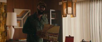 Movie still from “Alice” (2022), directed by Krystin Ver Linden – A man in a hat is holding up a record album; Medium shot, Over the shoulder angle