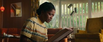 Movie still from “Alice” (2022), directed by Krystin Ver Linden – A woman sitting in front of an open book; Medium shot, Low angle