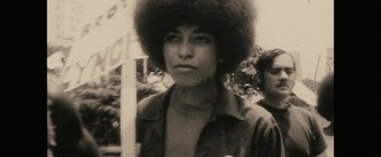 Movie still from “Alice” (2022), directed by Krystin Ver Linden – A young man with a large black afro is standing in front of a pole; Close Up shot, Low angle