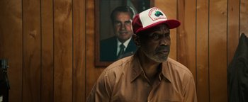 Movie still from “Alice” (2022), directed by Krystin Ver Linden – A man wearing a hat in front of a picture of a man; Close Up shot, Over the shoulder angle