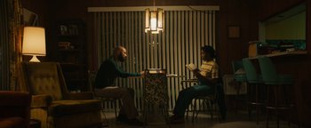 Movie still from “Alice” (2022), directed by Krystin Ver Linden – A man and a woman sitting at a table reading; Wide shot, High angle
