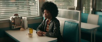 Movie still from “Alice” (2022), directed by Krystin Ver Linden – A person sitting at a table in front of a window; Medium shot, Over the shoulder angle