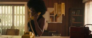 Movie still from “Alice” (2022), directed by Krystin Ver Linden – A woman talking on a phone while sitting at a table; Medium shot, Low angle