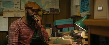 Movie still from “Alice” (2022), directed by Krystin Ver Linden – A man sitting at a desk talking on a phone; Medium shot, High angle