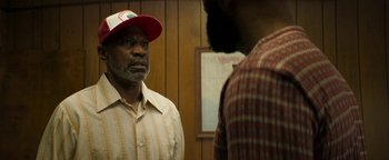 Movie still from “Alice” (2022), directed by Krystin Ver Linden – A man wearing a red hat and a striped shirt talking to another man in front of a wooden wall; Close Up shot, Over the shoulder angle