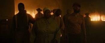 Movie still from “Alice” (2022), directed by Krystin Ver Linden – A group of people standing in front of a burning building; Medium shot, Low angle
