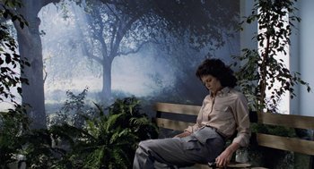Movie still from “Aliens” (1986), directed by James Cameron – A woman sitting on top of a wooden park bench; Wide shot, High angle