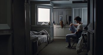 Movie still from “Aliens” (1986), directed by James Cameron – A man sitting in a chair next to a bed in front of a window; Wide shot, High angle