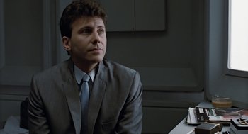 Movie still from “Aliens” (1986), directed by James Cameron – A man wearing a suit and tie sitting at a table; Close Up shot, Low angle
