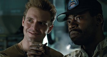 Movie still from “Aliens” (1986), directed by James Cameron – A man standing next to another man wearing a hat; Close Up shot, Low angle