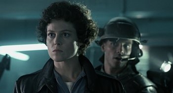 Movie still from “Aliens” (1986), directed by James Cameron – A woman standing next to a man wearing a helmet; Close Up shot, Low angle