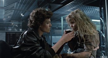 Movie still from “Aliens” (1986), directed by James Cameron – Two people are sitting at a table and one of them is holding a cup; Medium shot, Low angle