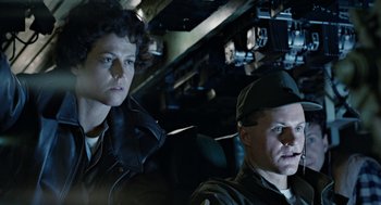 Movie still from “Aliens” (1986), directed by James Cameron – Two people sitting in a vehicle in a dark place; Medium shot, Low angle
