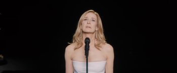 A woman in a white top is singing into a microphone