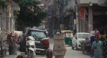 Movie still from “All That Breathes” (2022), directed by Shaunak Sen – A person walking down the street carrying boxes of food; Wide shot, Low angle