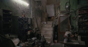 Movie still from “All That Breathes” (2022), directed by Shaunak Sen – A room filled with lots of junk and a staircase; Wide shot, High angle
