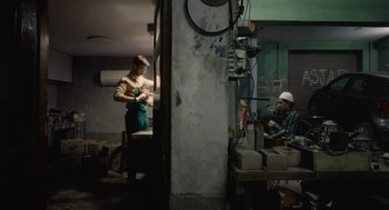 Movie still from “All That Breathes” (2022), directed by Shaunak Sen – A woman standing next to a man working in a factory; Wide shot, High angle
