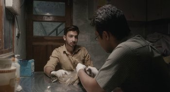 Movie still from “All That Breathes” (2022), directed by Shaunak Sen – A man wearing white gloves is talking to another man; Close Up shot, Low angle