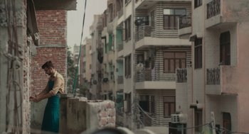Movie still from “All That Breathes” (2022), directed by Shaunak Sen – A person standing next to a building on the side of a road; Wide shot, Over the shoulder angle