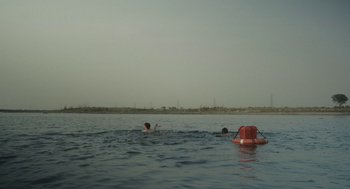 Movie still from “All That Breathes” (2022), directed by Shaunak Sen – Two people swimming in a body of water; Extreme Wide shot, High angle